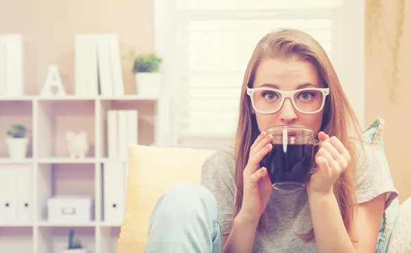Mulher feliz bebendo café em seu sofá — Fotografia de Stock