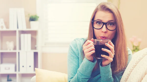 Mulher feliz bebendo café em seu sofá — Fotografia de Stock