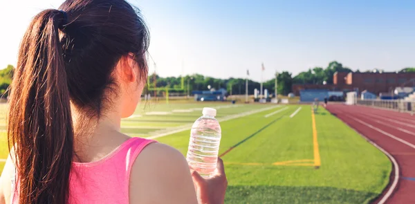 Female athlete drinking water on a running track
