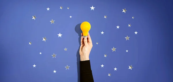 Person holding a yellow light bulb with stars — Stock Photo, Image