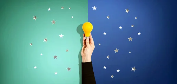 Persona sosteniendo una bombilla amarilla con estrellas — Foto de Stock