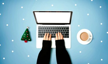 Yılbaşı ağacı yastığı ve bir fincan kahvesi olan bir dizüstü bilgisayar kullanan kişi.
