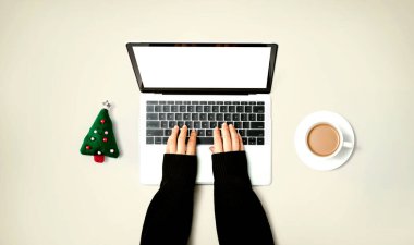 Yılbaşı ağacı yastığı ve bir fincan kahvesi olan bir dizüstü bilgisayar kullanan kişi.