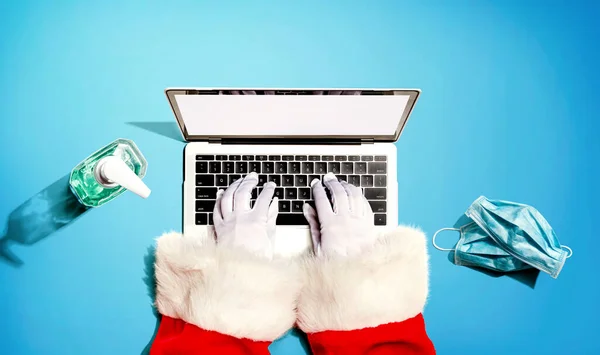Święty Mikołaj za pomocą laptopa z maską i butelką środka dezynfekującego — Zdjęcie stockowe
