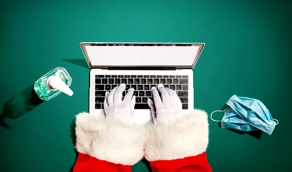 Santa Claus usando una computadora portátil con una máscara y una botella de desinfectante —  Fotos de Stock