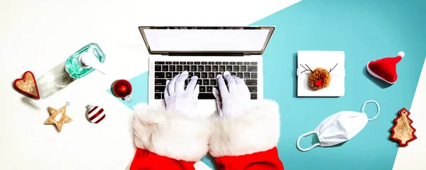 Санта Клаус использует ноутбук с маской и бутылкой дезинфицирующего средства — стоковое фото