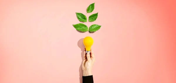 Persona sosteniendo una bombilla con hojas verdes — Foto de Stock