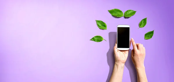 Pessoa segurando smartphone com folhas verdes — Fotografia de Stock