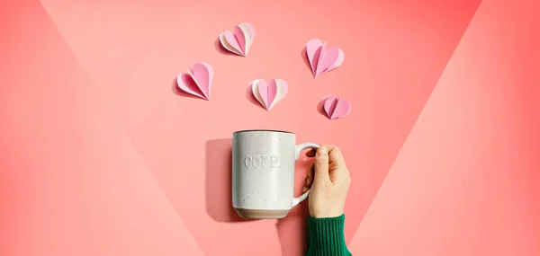Mano femenina sosteniendo una taza con corazones artesanales de papel —  Fotos de Stock