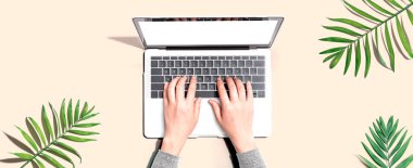 Tropikal yaprakları olan bir dizüstü bilgisayar kullanan kişi