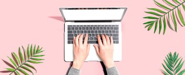 Tropikal yaprakları olan bir dizüstü bilgisayar kullanan kişi