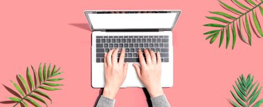 Tropikal yaprakları olan bir dizüstü bilgisayar kullanan kişi