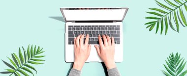 Tropikal yaprakları olan bir dizüstü bilgisayar kullanan kişi