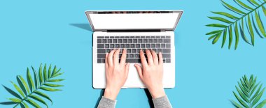 Tropikal yaprakları olan bir dizüstü bilgisayar kullanan kişi