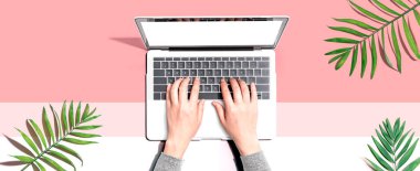 Tropikal yaprakları olan bir dizüstü bilgisayar kullanan kişi