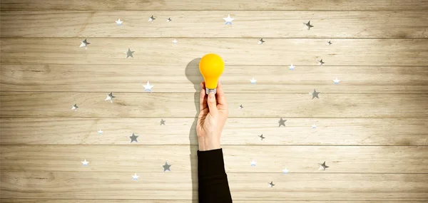 Persona sosteniendo una bombilla amarilla con estrellas — Foto de Stock