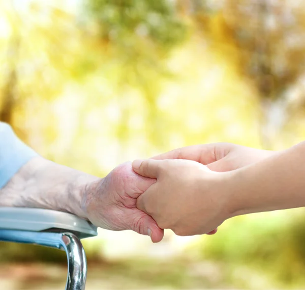 Seniorin im Rollstuhl hält Hand in Hand mit junger Hausmeisterin — Stockfoto