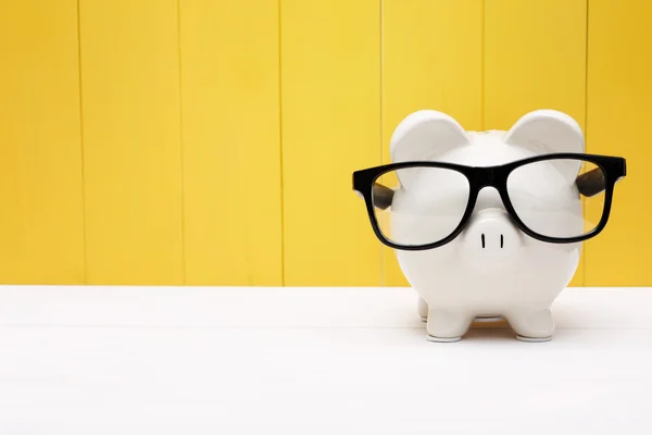 Banco Piggy com óculos sobre a parede de madeira amarela — Fotografia de Stock