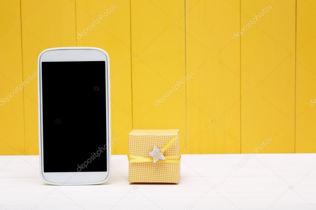 Cellphone and small gift box over yellow wood