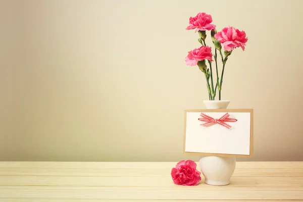 Claveles rosados en jarrón blanco con tarjeta de felicitación en blanco — Foto de Stock