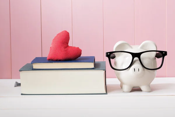 Piggy Bank with Glasses Beside Books with Heart — Stock Photo, Image