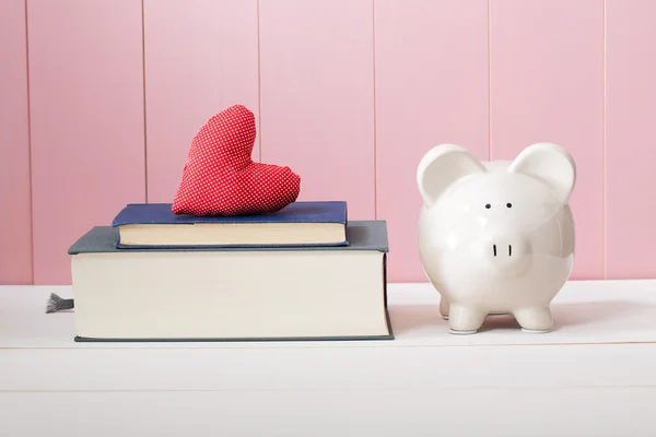 Sparschwein neben Büchern mit Herzkissen — Stockfoto