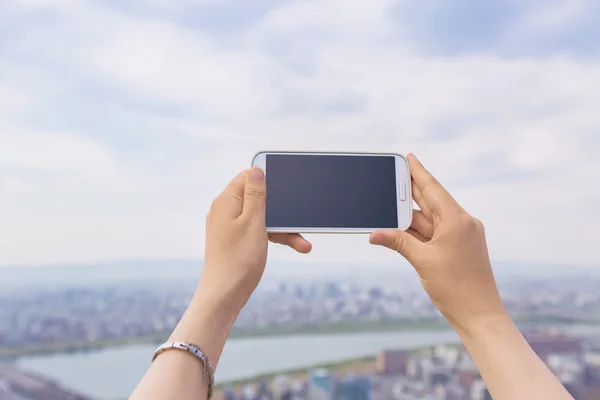 Person som innehar en mobil på staden bakgrund — Stockfoto