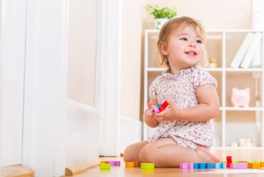 Gülümseyen ve ahşap oyuncak bloklarla oynama yürümeye başlayan çocuk
