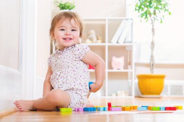 Ahşap oyuncak blokları ile oynarken gülümseyerek yürümeye başlayan çocuk kız