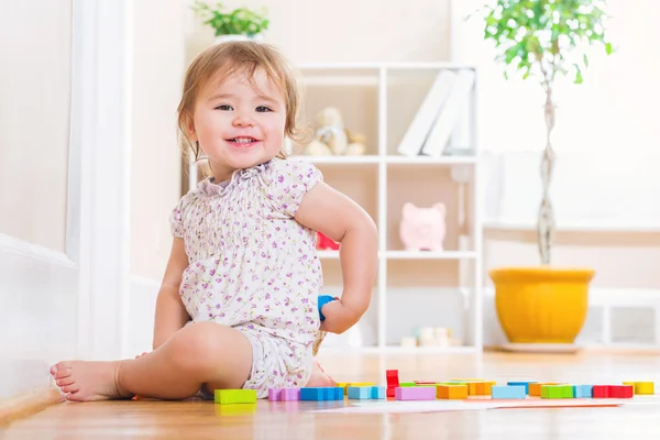 Toddler girl smiling while playing with wooden toy blocks — Stock Photo, Image
