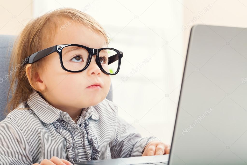 Intelligent toddler girl wearing big glasses while using her laptop