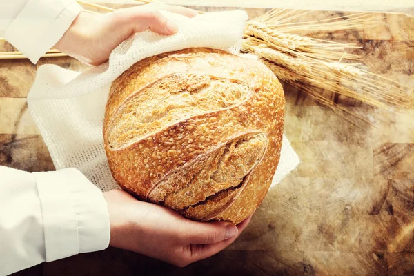 Baker sosteniendo una hogaza de pan sobre fondo rústico —  Fotos de Stock