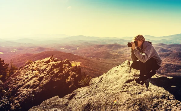 Homem com uma câmera no topo de um penhasco com vista para as montanhas — Fotografia de Stock