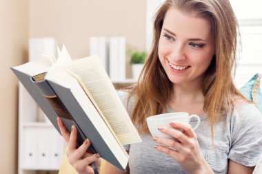 Mutlu genç kadın onun kanepenin üzerine bir kitap okuma 