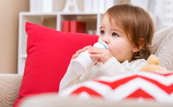 Barn girl dricka mjölk på hennes soffa — Stockfoto