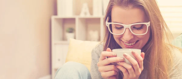 Jonge vrouw drinken koffie op haar bank — Stockfoto