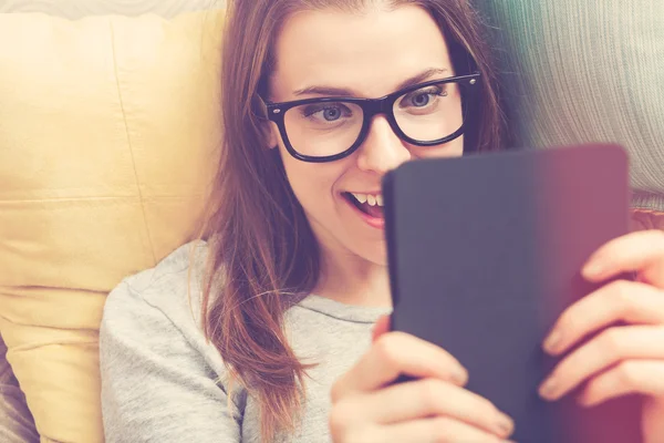 Ung kvinna läser en e-bok på hennes soffa — Stockfoto