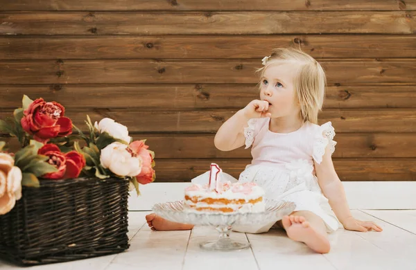 little beautiful blue-eyed girl celebrates her first birthday in the style smash a cake and she tastes her first birthday cake
