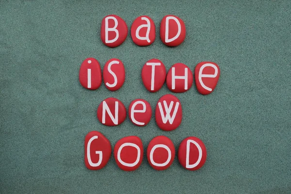 Bad is the new good, creative slogan composed with red colored stone letters over green sand