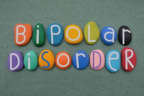 Bipolar disorder, mental health condition composed with multi colored stone letters over green sand