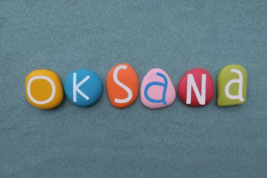 Yeşil kumların üzerinde el yapımı çok renkli taş harflerle Oksana adında bir kadın için yaratıcı bir kompozisyon.