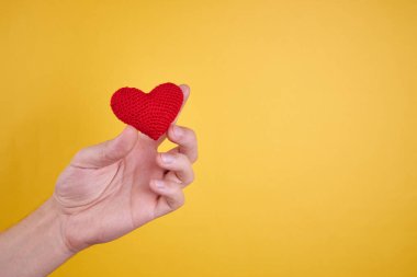 Erkek kişinin elinde sarı arka planda izole edilmiş kalp sembolü var. Romantizm ve Sevgililer Günü konsepti