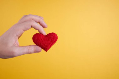 Erkek kişi kırmızı kalbi sarı arka planda tek başına tutuyor. Romantizm ve Sevgililer Günü konsepti