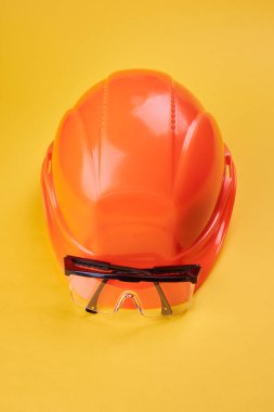 Parlak sarı arka planda turuncu koruyucu başlık ve güvenlik gözlüğü var. dikey yönelim. Koruyucu iş giyimi ve inşaat endüstrisi kavramı