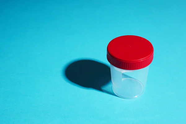 Klinik test için tıbbi örnek konteynırı. Kırmızı bardaklı boş bir şişe ve mavi arka planda sert bir gölge. Boşluğu kopyala