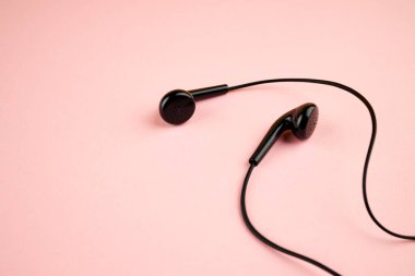 Pembe pastel arka planda izole edilmiş siyah kulaklık. Düz yat. Uzay boşluğu. müzik konsepti