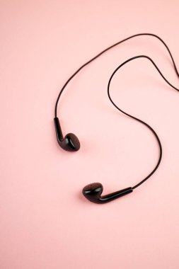 Pembe pastel arka planda izole edilmiş siyah kulaklık. Düz yat. Uzay boşluğu. müzik minimalizmi