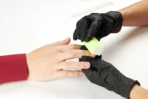 Manicura durante el trabajo usando uñas de buff. un proceso de manicura del hombre. una persona caucásica irreconocible haciendo servicio de uñas en el salón de spa. — Foto de Stock