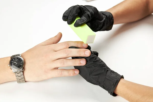 Manicura durante el trabajo usando uñas de buff. un proceso de manicura del hombre. una persona caucásica irreconocible haciendo servicio de uñas en el salón de spa. — Foto de Stock