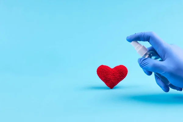 medical heart treatment. person with blue latex gloves use sanitizer for heart symbol over blue background. copy space